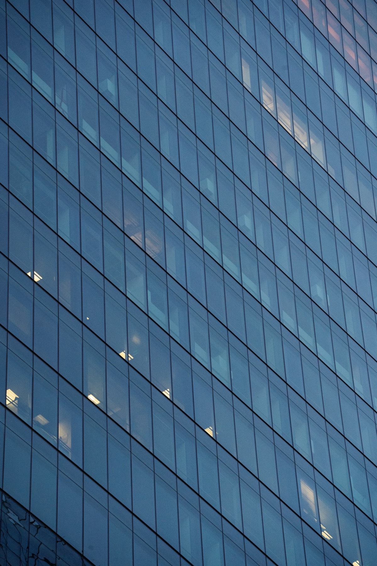 Blue glass facade of an office tower with a few lit windows